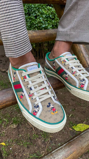 On-foot outdoor view of Gucci x Disney Mickey Mouse Tennis 1977 low-top sneakers worn with jeans.