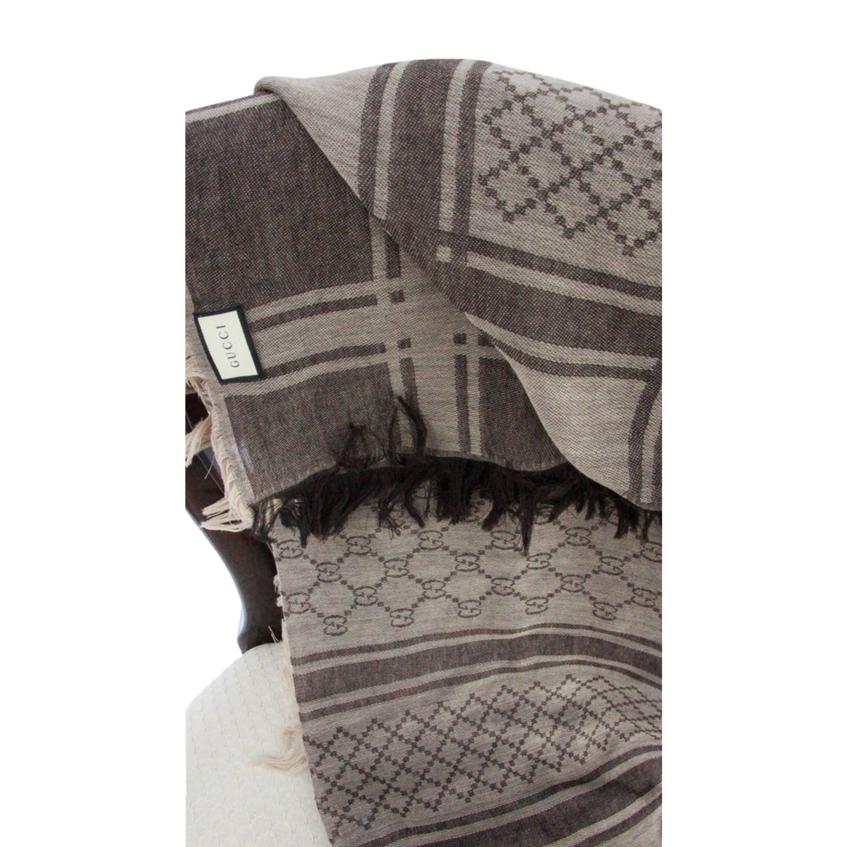 Vertical view of folded brown Gucci GG monogram wool scarf displaying classic pattern layout and frayed edges.