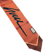 Detailed view of the Gucci cursive logo signature and lipstick motif on the orange and blue silk scarf.