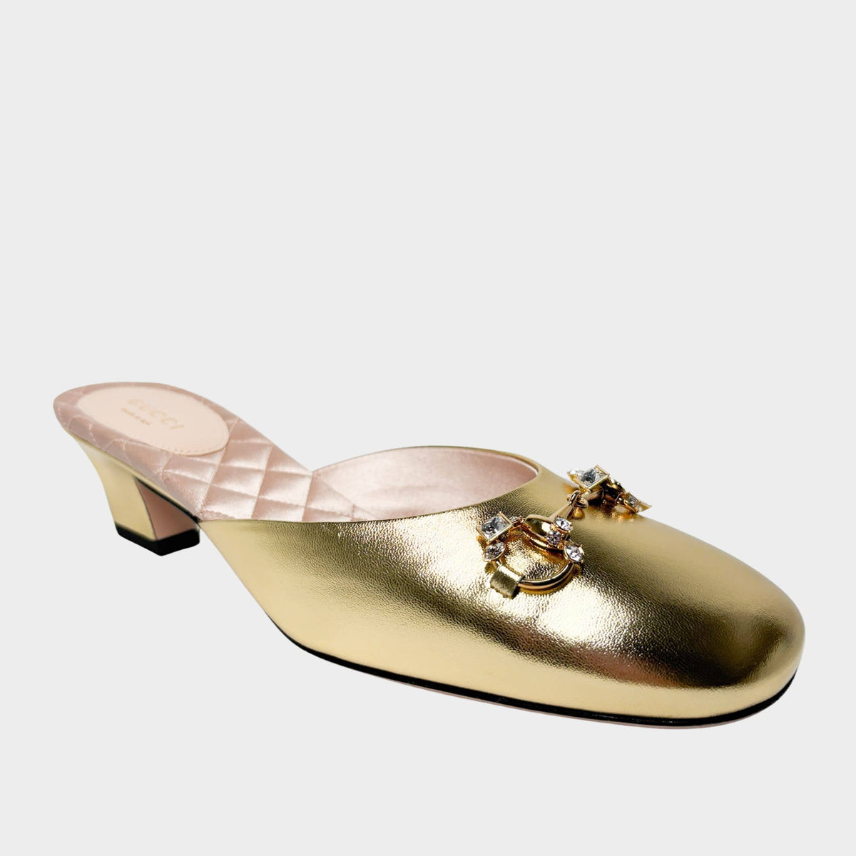 Side profile view of a Gucci mule in metallic gold leather, showcasing the low quilted block heel and the sparkling diamond-embellished Horsebit hardware.