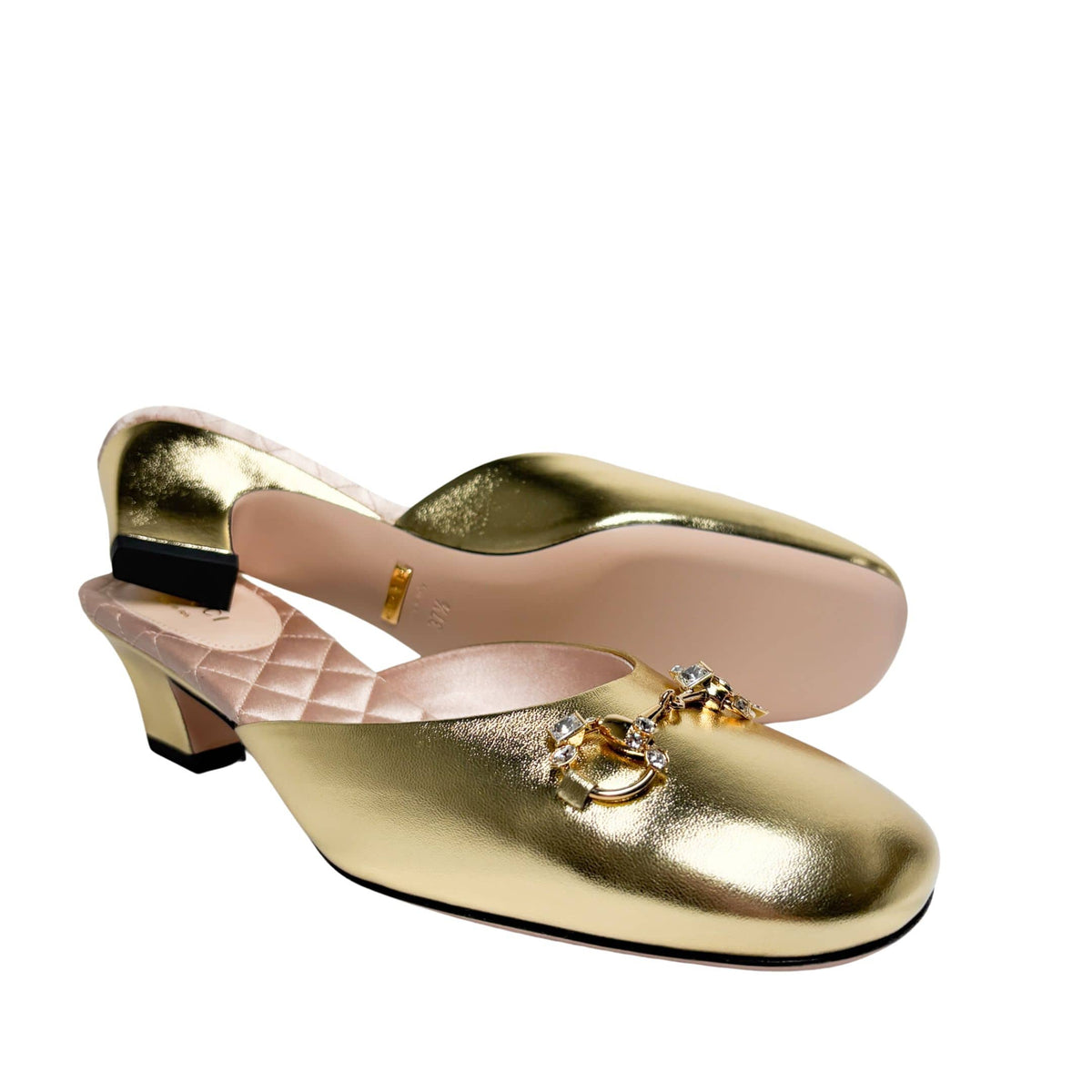 Side perspective of both gold Gucci mules arranged in parallel, showing the contrast between the black outsole and the metallic gold upper.