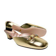 Side perspective of both gold Gucci mules arranged in parallel, showing the contrast between the black outsole and the metallic gold upper.