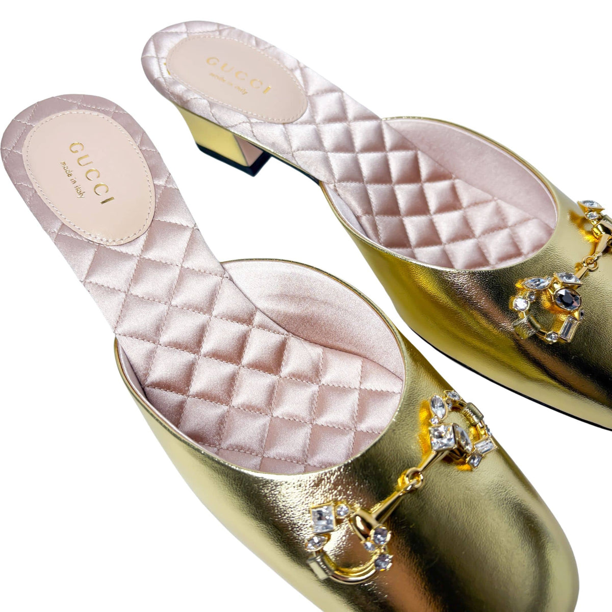 Top-down angled view of the gold Gucci mules, displaying the soft pink quilted leather insoles and debossed Gucci logo branding.