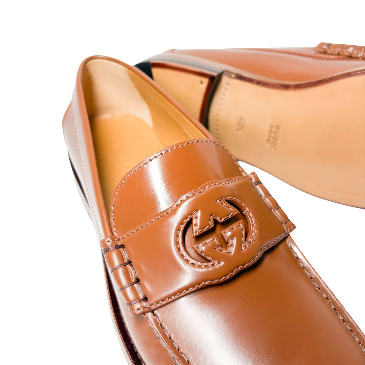 Close-up macro shot of Gucci Millennial Ribot brown loafer strap featuring embossed GG logo detail and smooth leather finish.