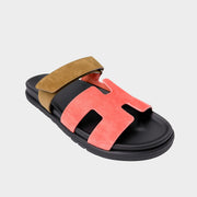 A side profile view of the Hermès Chypre sandal showcasing the bold contrast between its vibrant coral-red leather upper and the thick black rubber sole.