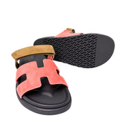 Close-up catalog presentation of the Hermès Chypre collection in Rouge Tomette, styled with one sandal overlapping the other to display the textured outsole edges.