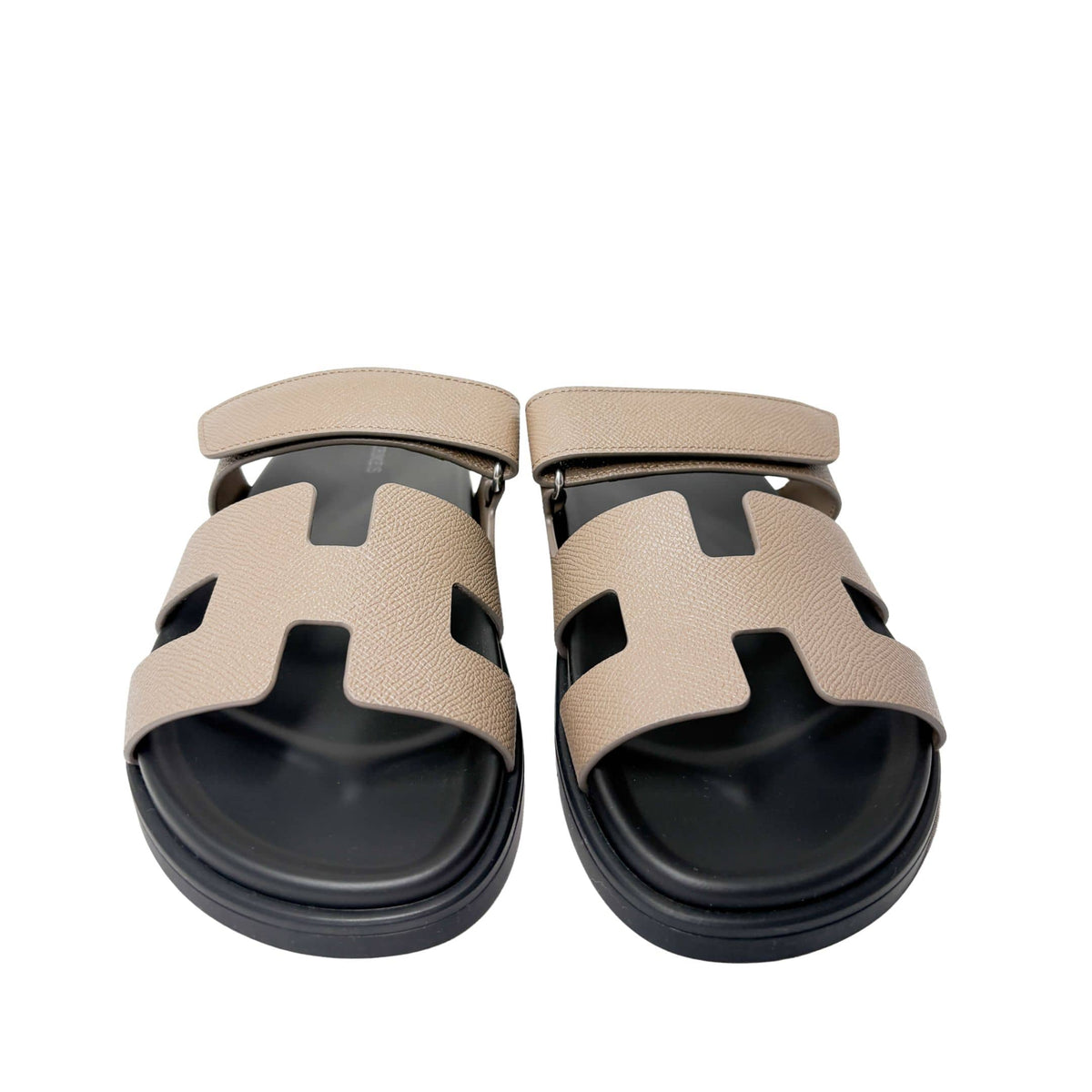 Symmetrical front-facing studio view of a pair of Etoupe Hermès Chypre sandals side-by-side, emphasizing the open toe box and black rubber sole.