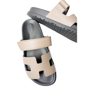 Asymmetrical studio shot of both Etoupe Hermès Chypre sandals overlapping, showcasing the fine edge painting and premium craftsmanship.