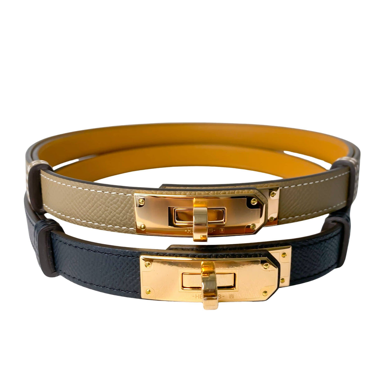 Stacked display of authentic Hermès adjustable Kelly belts in Étoupe taupe-grey, beige, and black leather