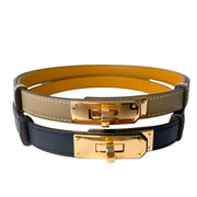 Stacked display of authentic Hermès adjustable Kelly belts in Étoupe taupe-grey, beige, and black leather