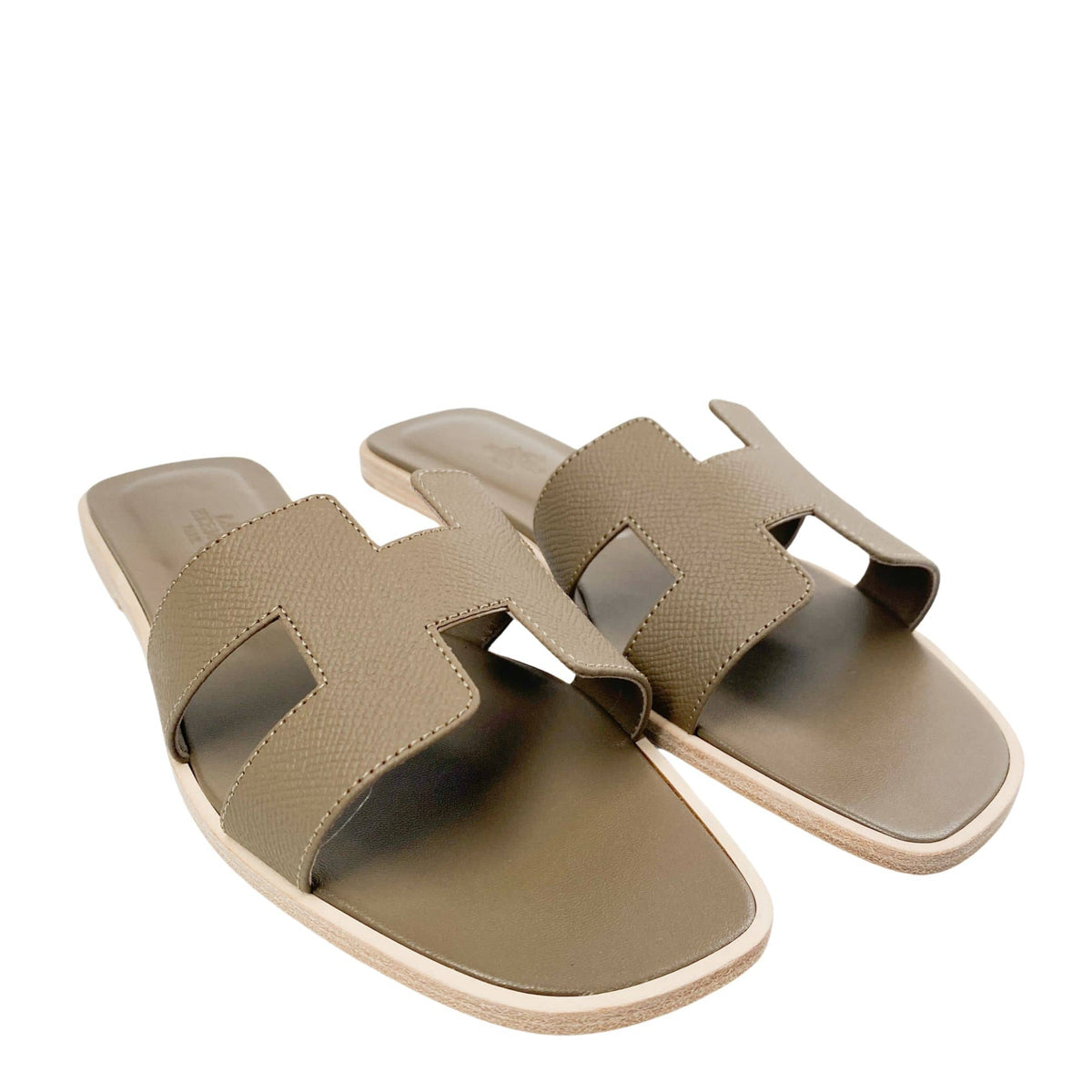 A parallel studio arrangement of the Étoupe calfskin sandals, highlighting how the signature topstitching outlines the clean silhouette of both open-toe flats against a neutral backdrop.