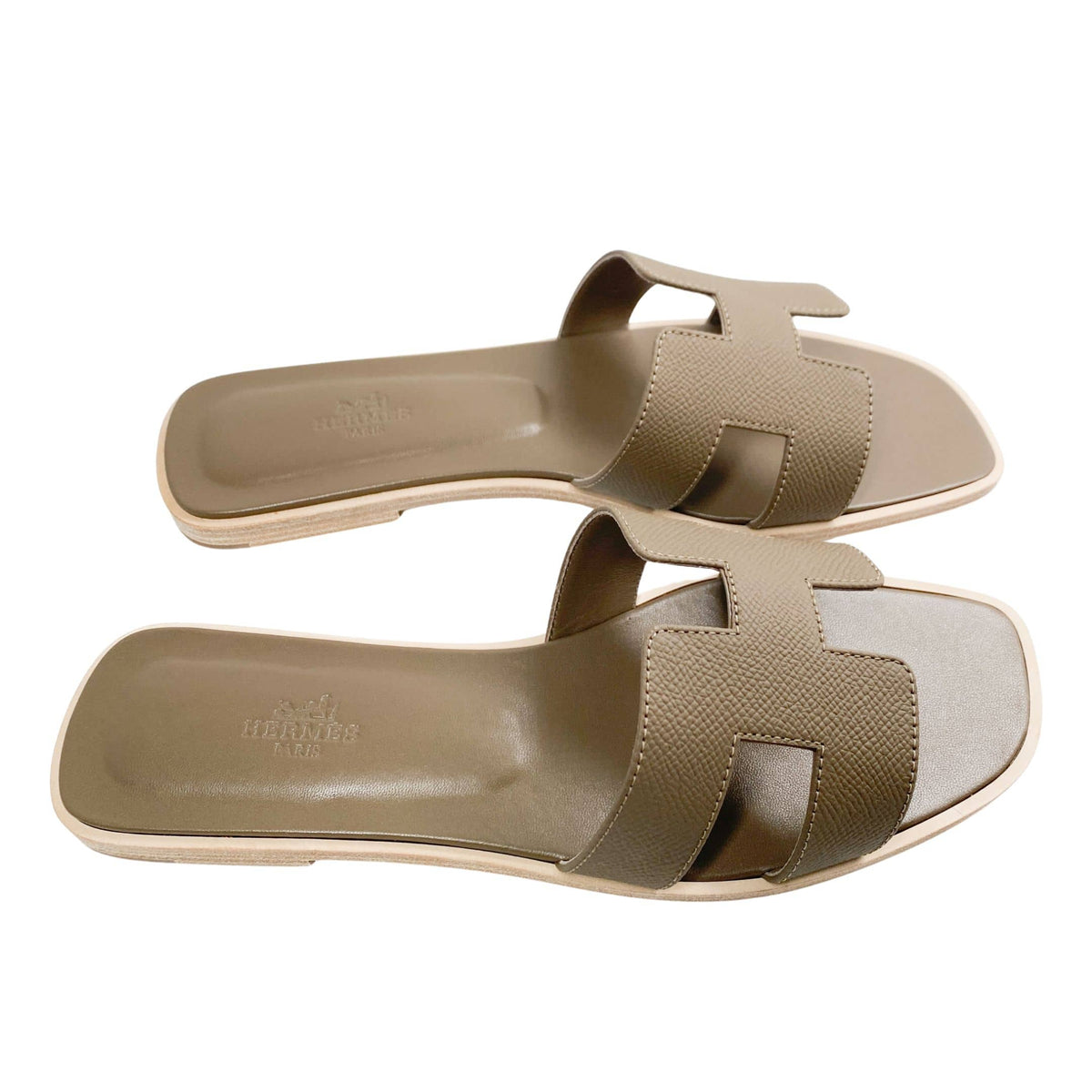 A direct glance at the inner footbeds of the flat Hermès summer slides, showcasing the branded luxury stamping and the ergonomic curvature made for daily wear