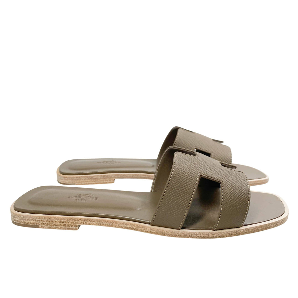 A level, horizontal profile view emphasizing the ultra-flat composition of the luxury Parisian sandal and the contrasting dark underside of its stacked heel.