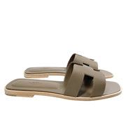 A level, horizontal profile view emphasizing the ultra-flat composition of the luxury Parisian sandal and the contrasting dark underside of its stacked heel.