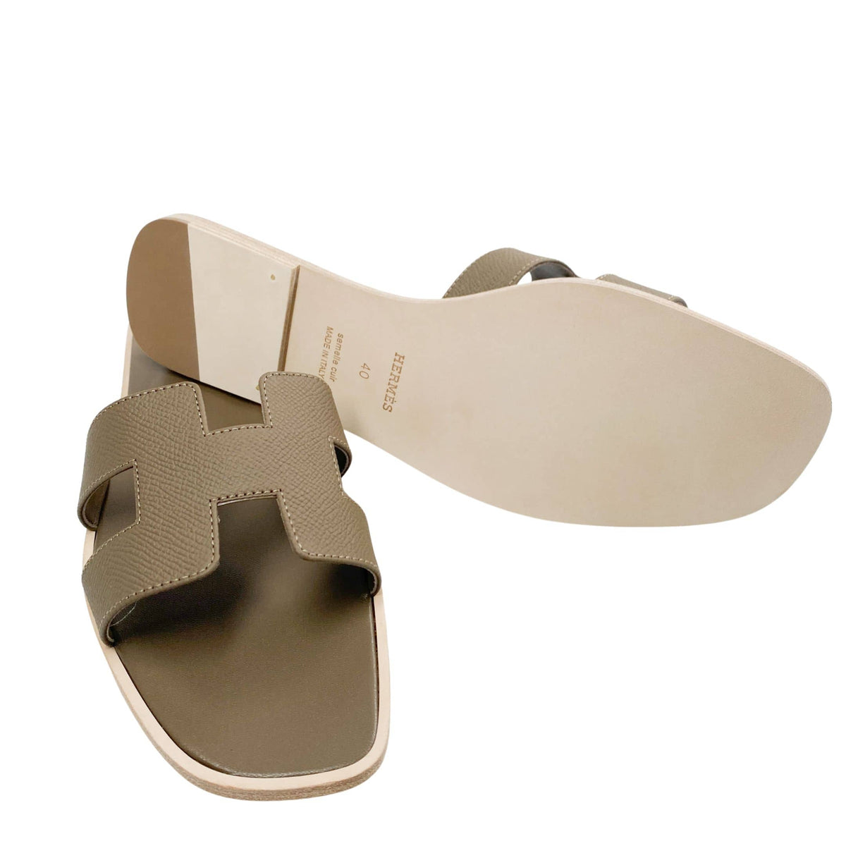 A dynamic composition showing one Étoupe leather sandal flipped over to document the artisan craftsmanship, detailed sizing marks, and smooth leather texture of the outsole.