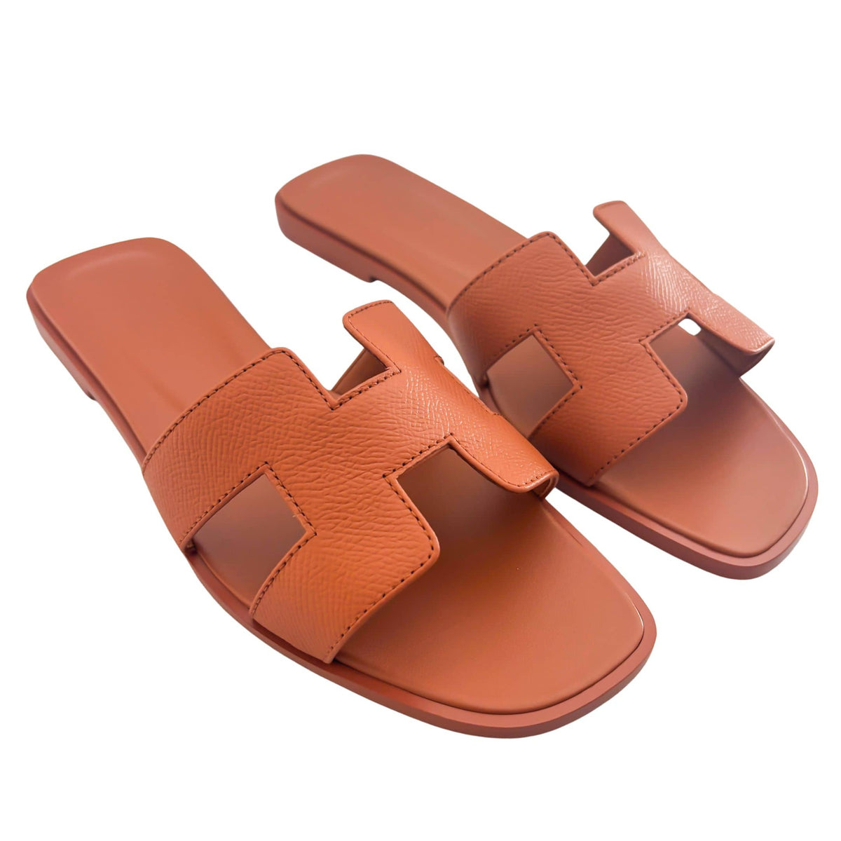 A side-by-side parallel arrangement of the orange leather Hermès sandals, emphasizing the clean edges of the iconic H cutout design.