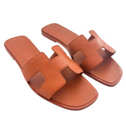 A side-by-side parallel arrangement of the orange leather Hermès sandals, emphasizing the clean edges of the iconic H cutout design.