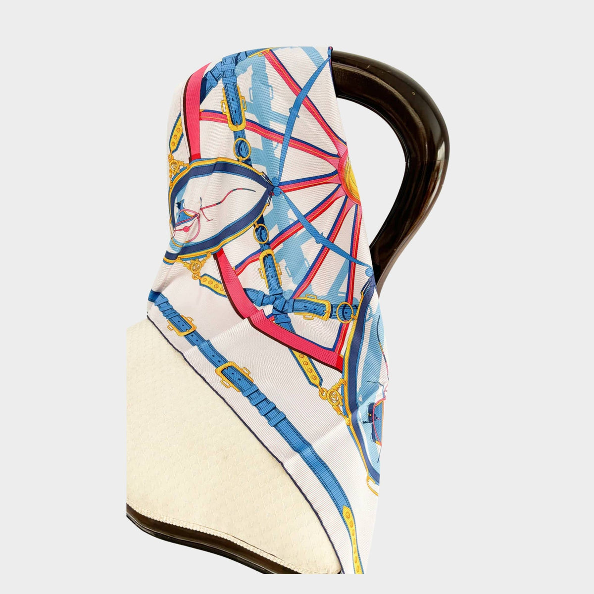 Authentic Hermès En Roue Libre Carré 90 silk scarf in cream with vibrant pink and blue carriage wheel design draped on display