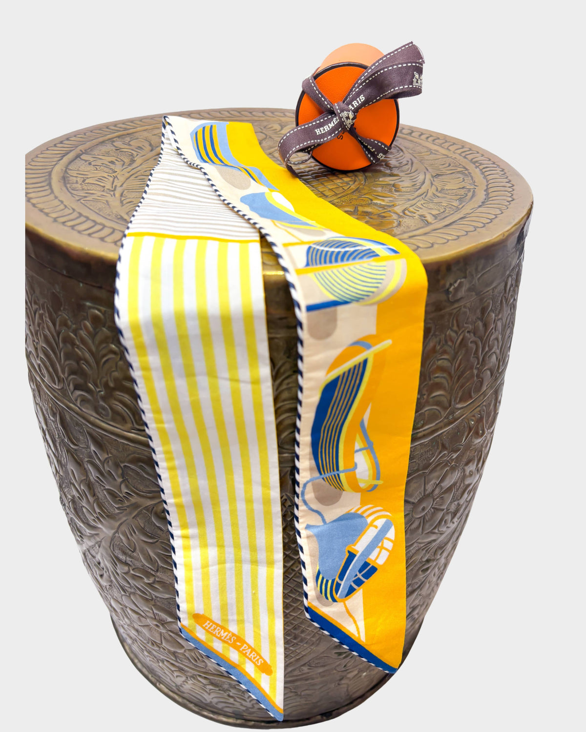 Hermès Thalassa cotton Twilly ribbon in bright yellow and white boat stripes draped over a textured wooden pedestal