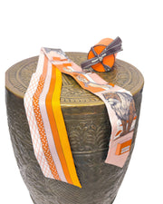 Side angle display of Hermès Grand Théâtre Nouveau silk Twilly scarf wrapped around a textured pedestal