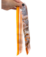 Full-length view of Hermès silk Twilly scarf in Grand Théâtre Nouveau print held up to showcase the slim silk design