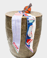 Hermès Thalassa cotton Twilly ribbon with nautical blue stripes and multi-color pattern draped over a textured wooden pedestal