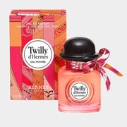 Twilly d'Hermès Eau Poivrée Eau de Parfum bottle with black bowler cap and silk ribbon displayed next to its pink patterned retail packaging box.