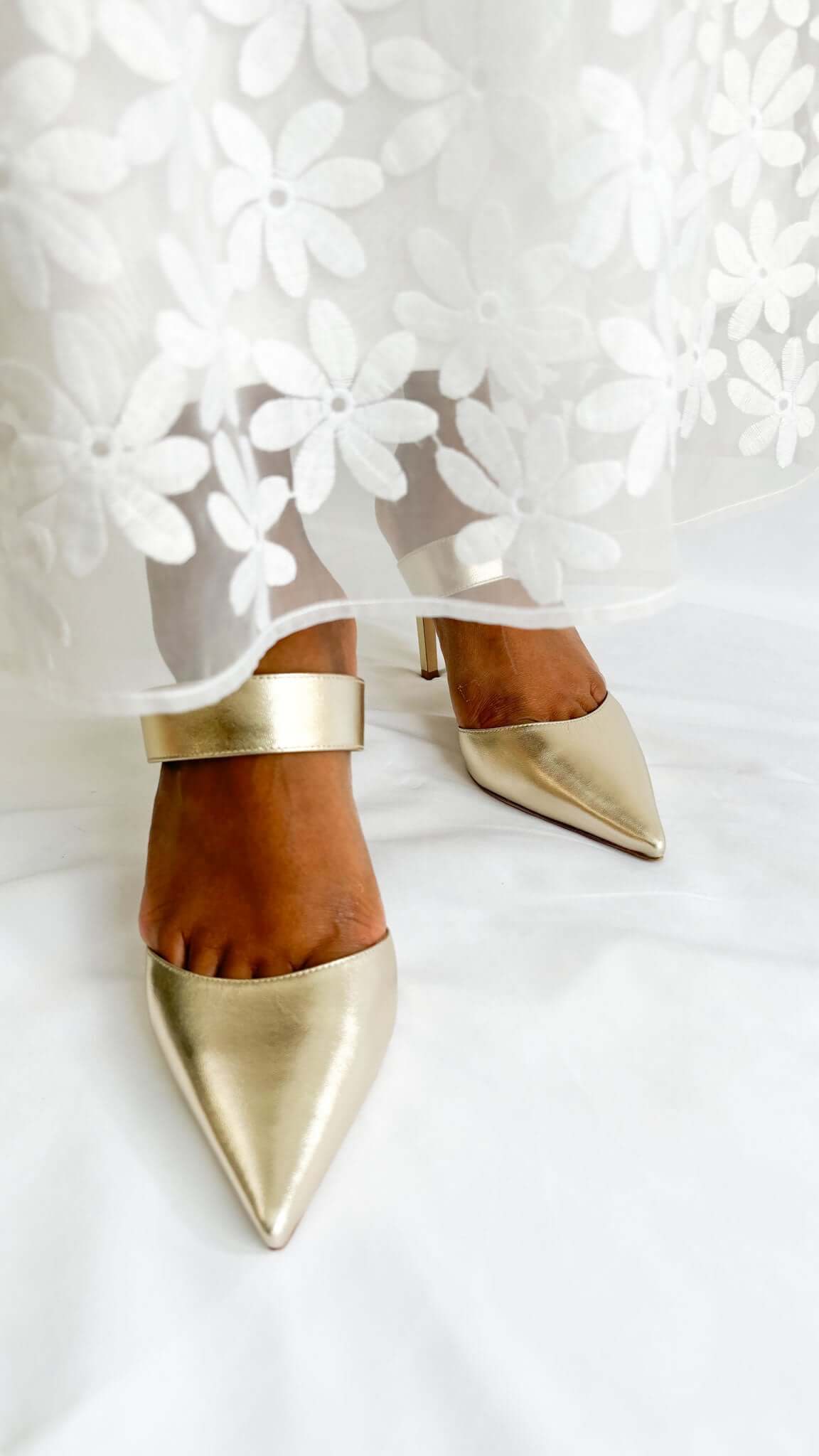 Front view of Jimmy Choo Cheri 85 metallic gold heels styled on foot with a white lace wedding dress.