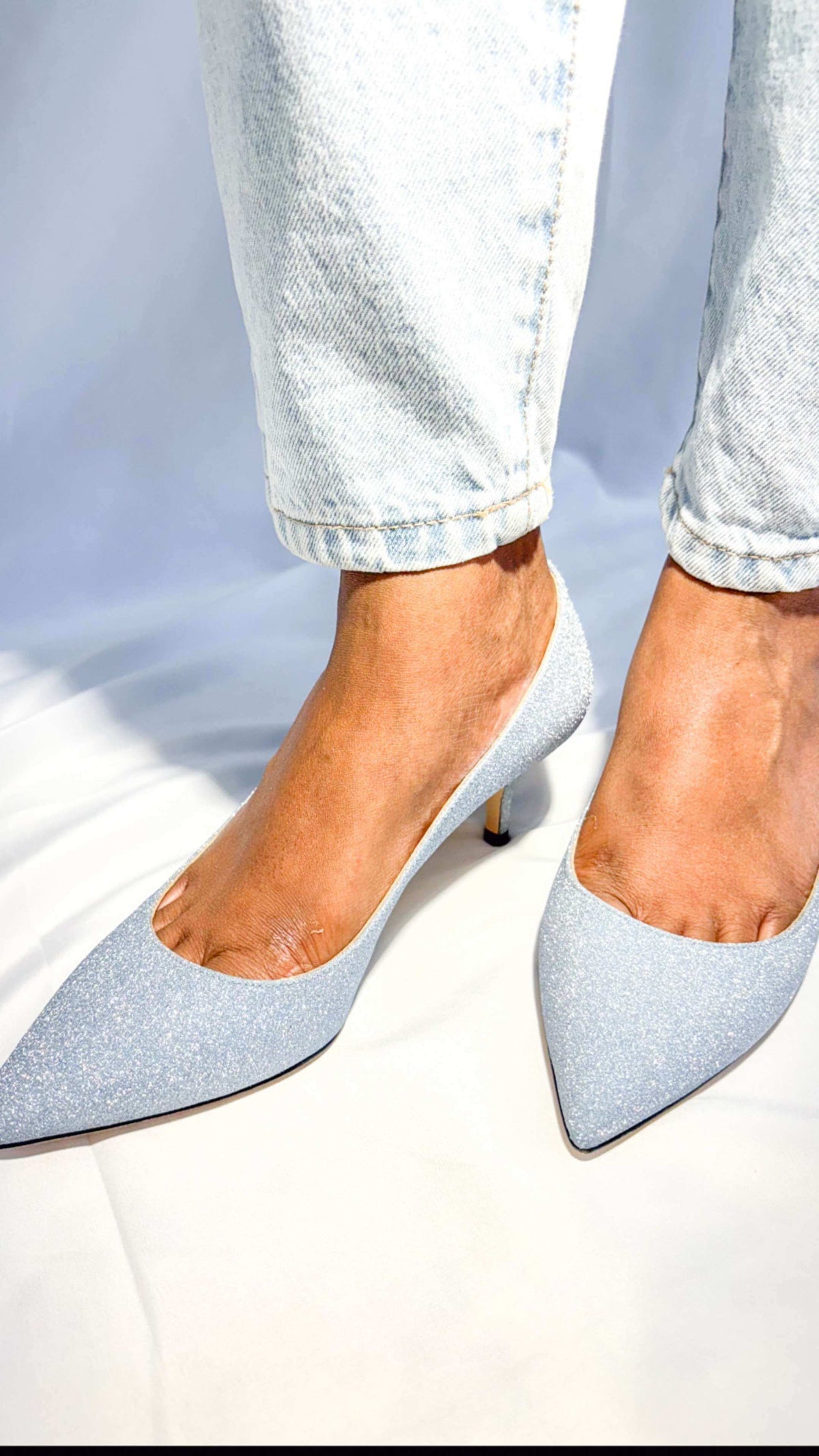 Angled on-foot perspective of Jimmy Choo Aza 50 light blue glitter pumps showcasing the elegant pointed toe box.