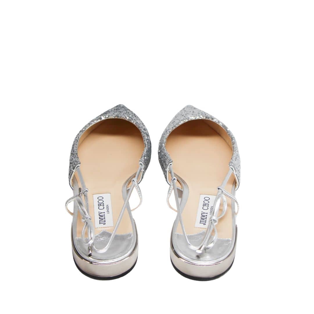 Overhead top-down view of a pair of Jimmy Choo Gemista silver glitter flats highlighting the pointed toe box and beige leather lining.