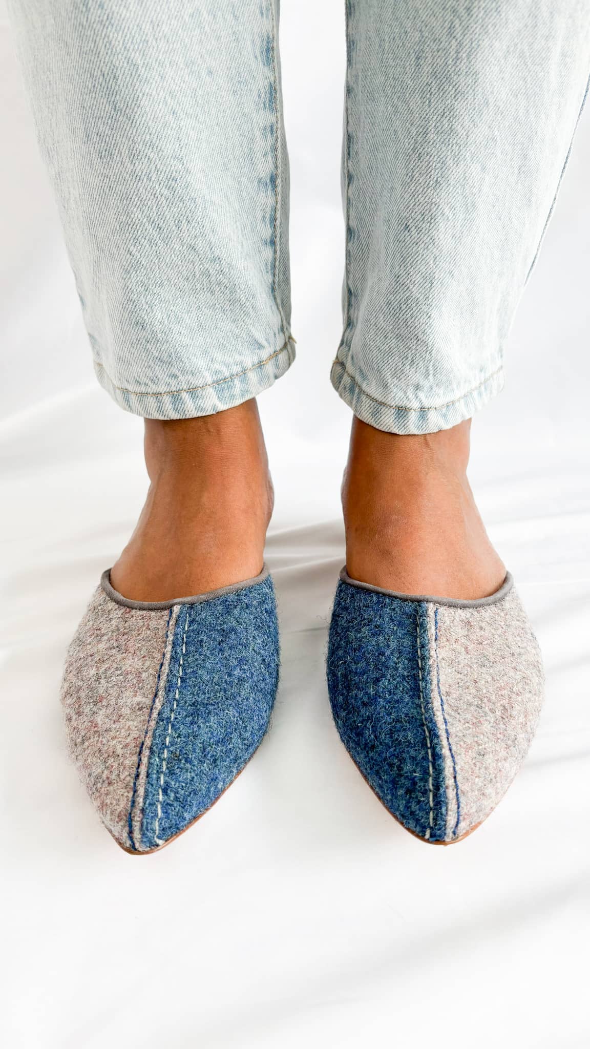 Direct front view on foot of Manolo Blahnik Ajita 30 grey and dark blue wool felt mules styled with light blue denim jeans.