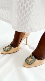 Front perspective view on foot of Manolo Blahnik Hangisi 105 champagne satin high heels styled with a white lace dress.