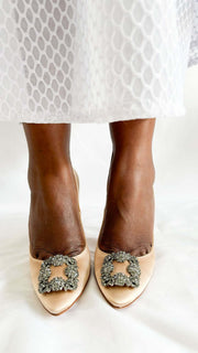 Direct front view on foot of Manolo Blahnik Hangisi 105 champagne pumps showcasing the signature gunmetal-encased crystal buckle.
