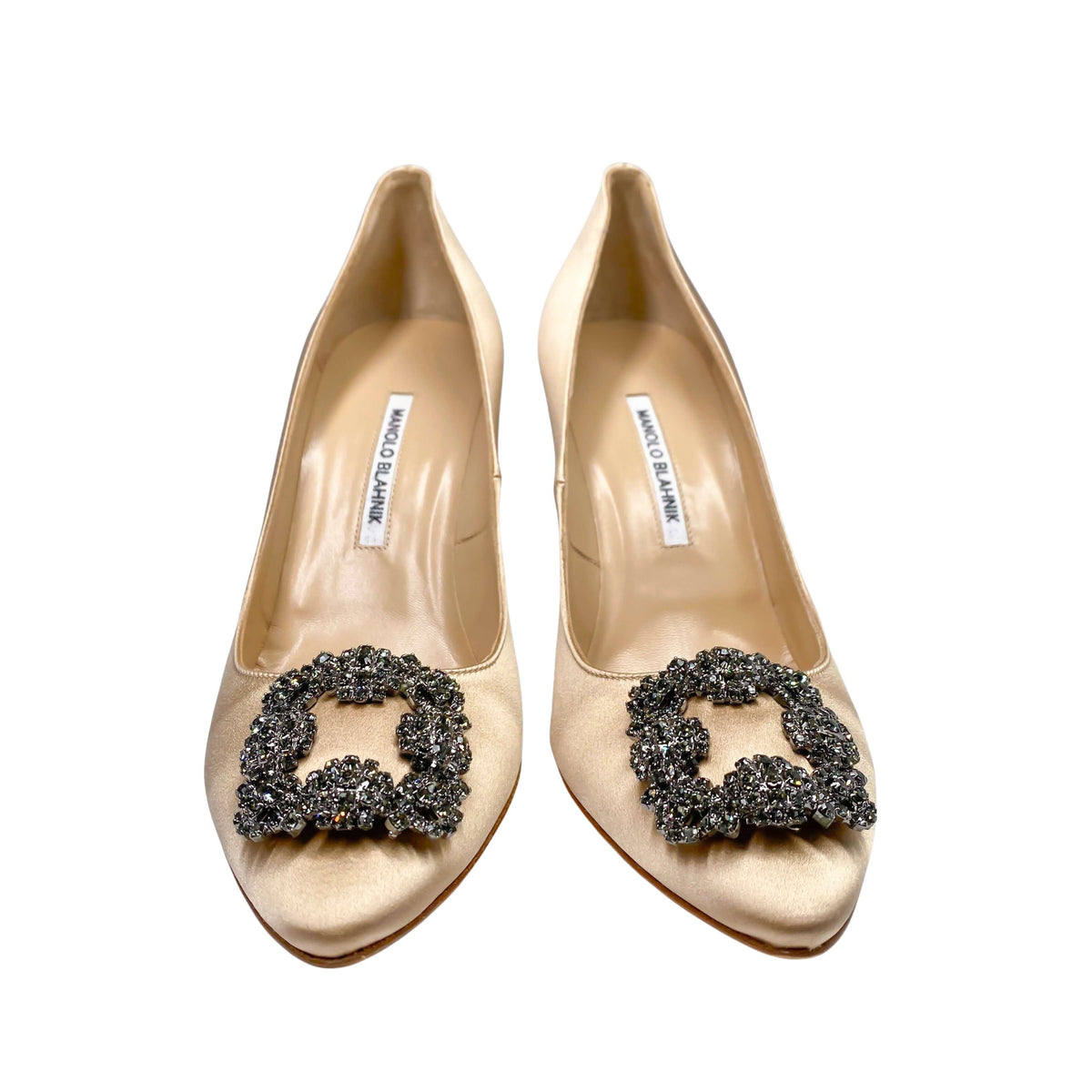 Studio side profile of Manolo Blahnik Hangisi 105 champagne satin pump showing the elegant heel curve and jewel buckle.