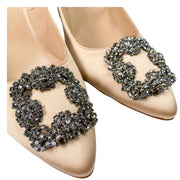 Close-up detail view of the iconic square crystal buckle and almond toe box on Manolo Blahnik Hangisi champagne satin pumps.