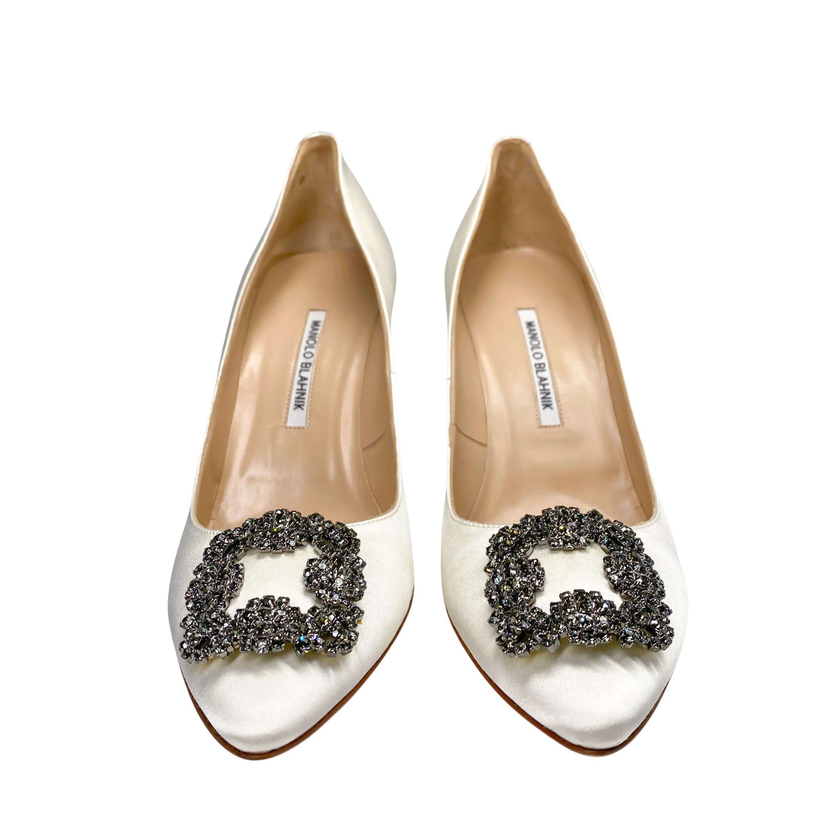 Top-down studio view of the Manolo Blahnik Hangisi white satin pumps showing the beige leather lining and insoles.