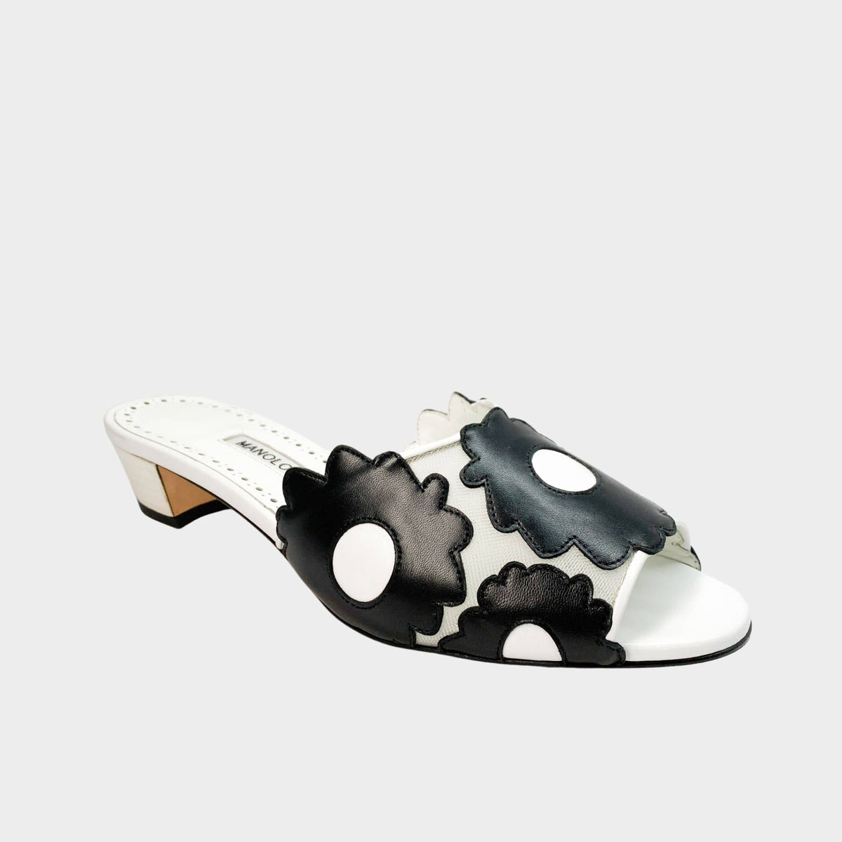 Side profile view of Manolo Blahnik Lottara 30 slide sandals in black and white leather featuring floral cutout overlays and a 30mm low block heel.