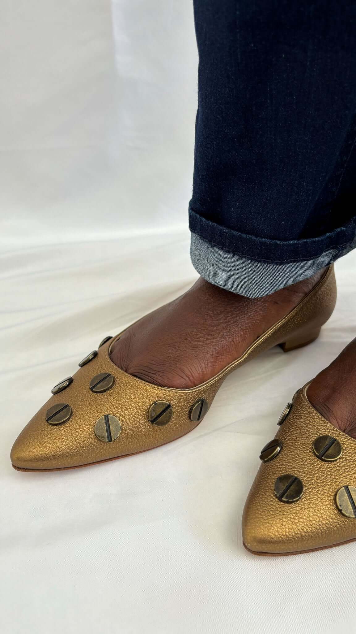 Three-quarter view of a pair of Manolo Blahnik Panunzia metallic bronze screw-accent flats on-foot.