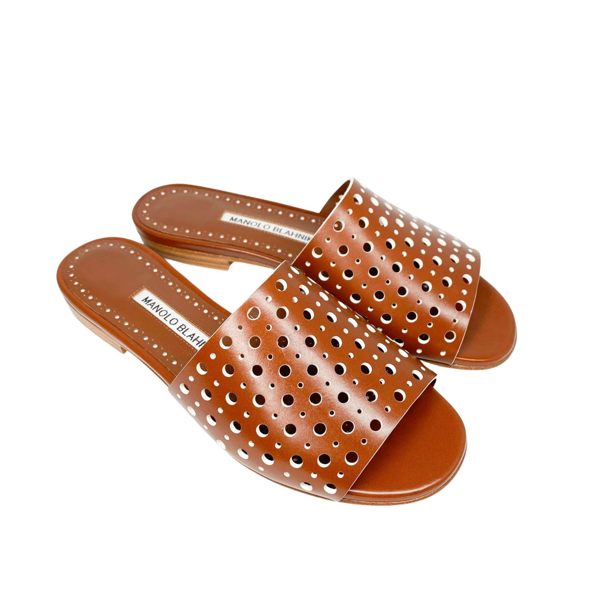 Three-quarter studio view of a pair of Manolo Blahnik Prepona tan brown cutout leather flat slides on a white background.