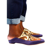 Side view of a person wearing Manolo Blahnik Abukov purple and gold satin slip-on flats with cropped denim jeans.