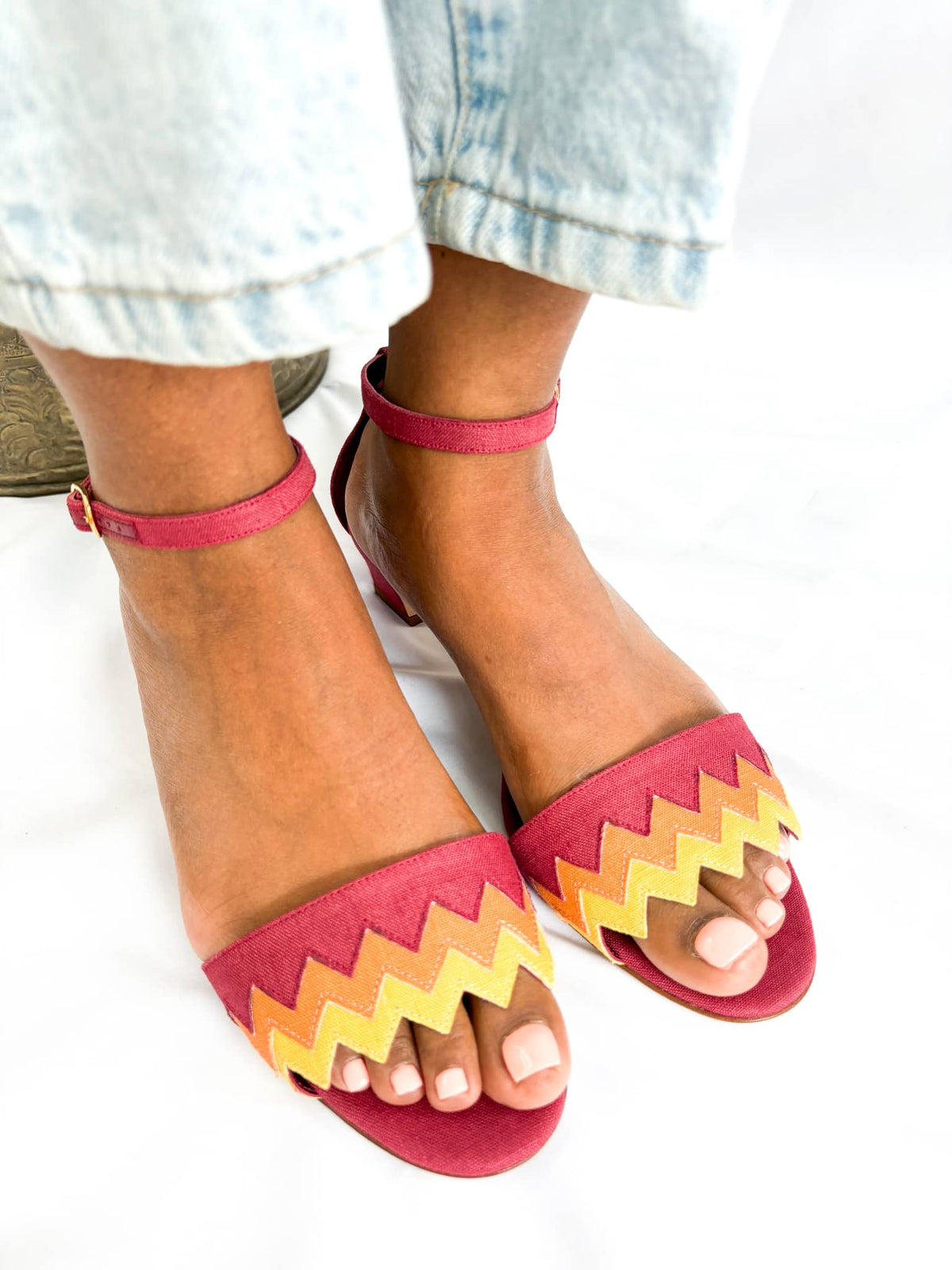 On-foot direct front view of Manolo Blahnik Lochpri red canvas zig-zag sandals styled with light wash cuffed denim jeans.