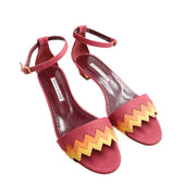 Three-quarter studio view of a pair of Manolo Blahnik Lochpri canvas ankle-strap sandals displaying yellow and orange zig-zag vamp details.