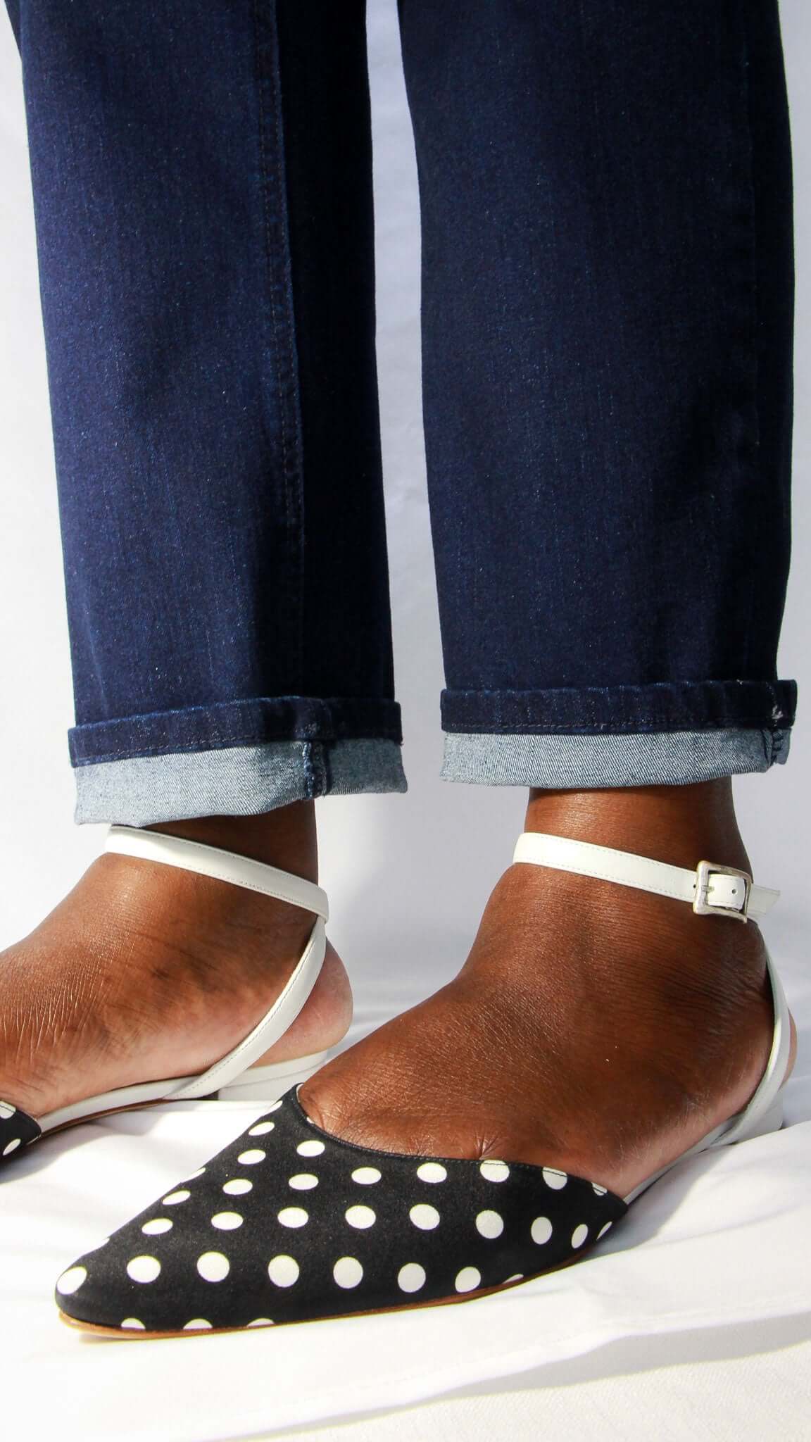 Close-up of a person styling Manolo Blahnik black and white polka dot pointed flats with denim.