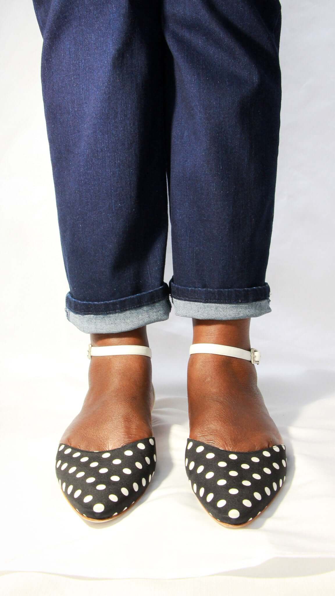 Top-down view of a person wearing Manolo Blahnik Asenso polka dot ankle strap flats with blue jeans.
