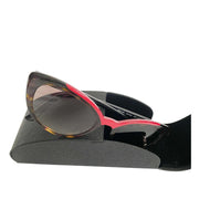 Prada cat-eye tortoise shell and red sunglasses displayed next to an authentic black Prada hard leather case