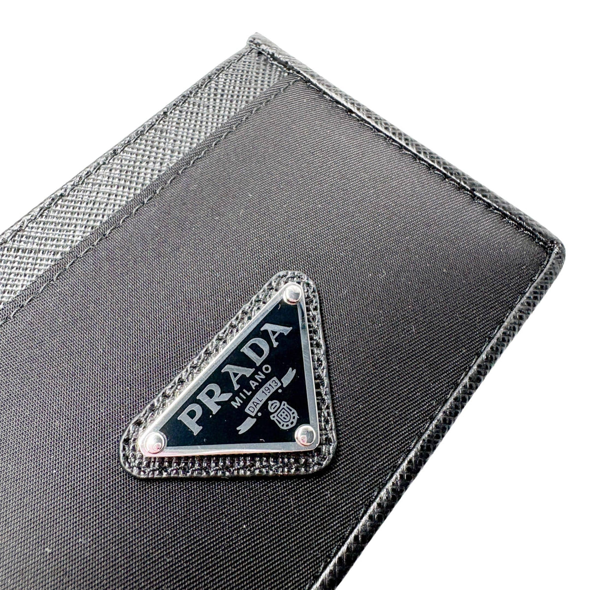 Close-up detail of silver-toned metal and black enamel Prada triangle logo on textured Saffiano leather