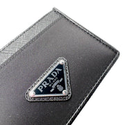 Close-up detail of silver-toned metal and black enamel Prada triangle logo on textured Saffiano leather