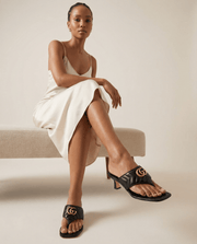 Model wearing the black leather Gucci Charlotte thong sandals in a minimalist photo studio setting, highlighting the elegant square toe line.