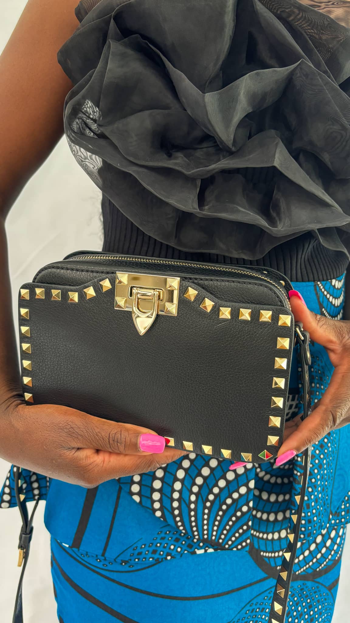 Model holding the black Valentino Rockstud camera bag closely in hand as a clutch.