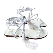 Three-quarter view of a pair of Valentino Garavani Flair white leather flat sandals with feather detail and ankle ties.